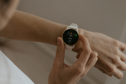 Pessoa ajustando smartwatch branco no pulso, tela exibindo monitoramento de batimentos cardíacos e atividade física.