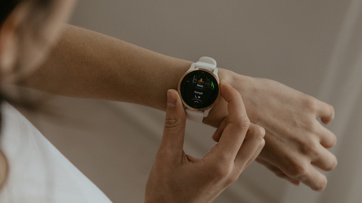 Pessoa ajustando smartwatch branco no pulso, tela exibindo monitoramento de batimentos cardíacos e atividade física.
