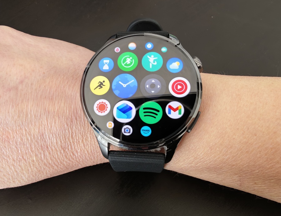 Smartwatch on a wrist displaying a grid of colorful app icons on its round touchscreen.