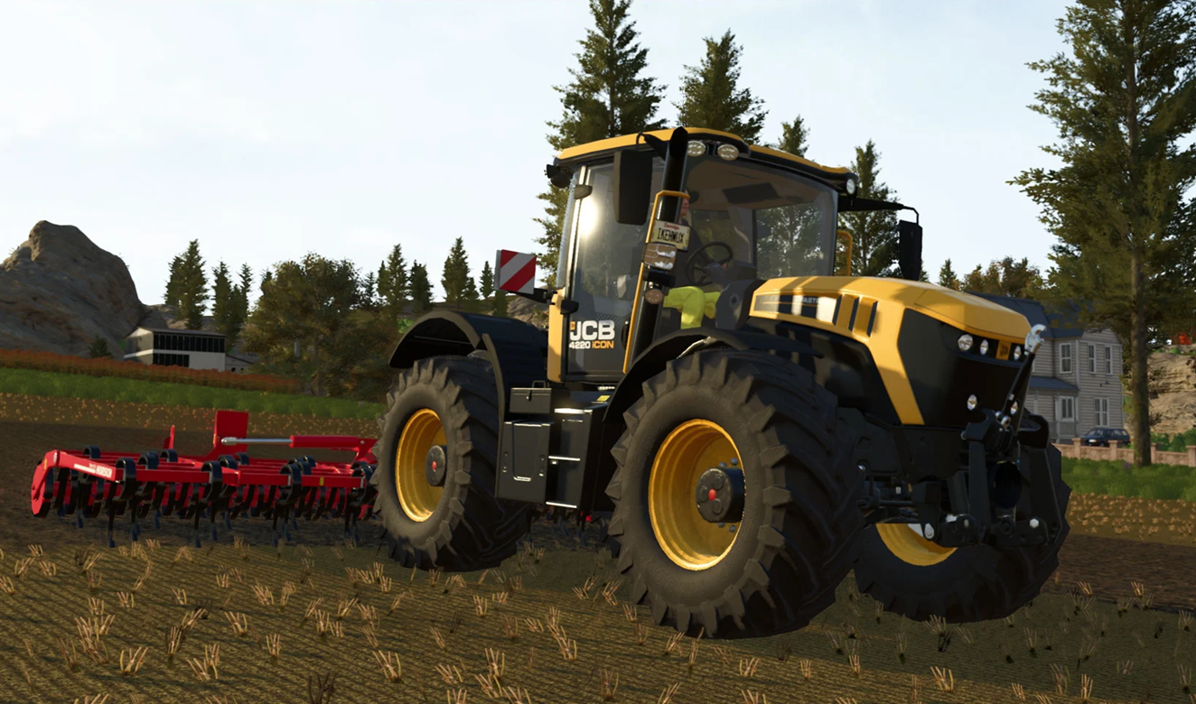 Yellow JCB tractor with large off-road tires pulling red cultivator in a harvested field with trees and farm buildings in the background.