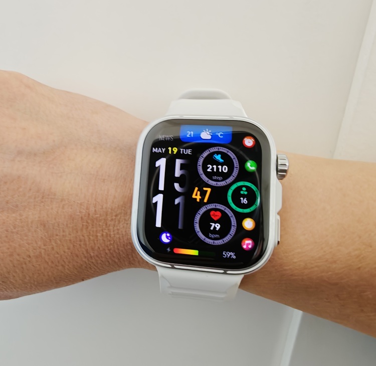 White smartwatch on a wrist with a colorful Apple Watch face showing time 15:11 and activity data (steps, heart rate, rings) in a bright, app-dense display.