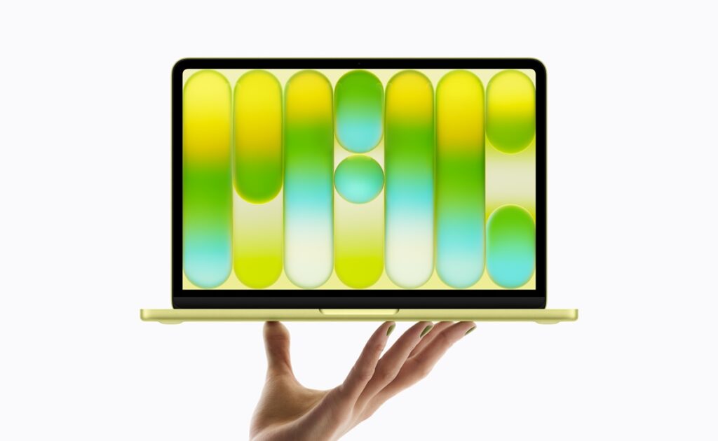 Hand supporting a gold laptop displaying a screen filled with large colorful capsules (pills).