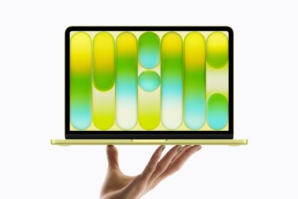 Hand supporting a gold laptop displaying a screen filled with large colorful capsules (pills).