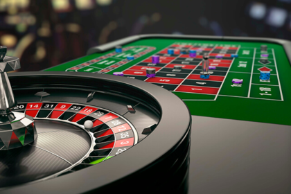 Roulette wheel in the foreground with a green casino betting table and chips in the background.