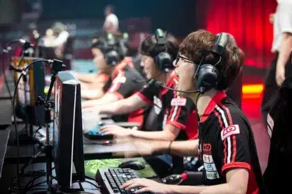 Pro esports team in a row, players wearing headsets and playing on desktop PCs with keyboards and mice during a match