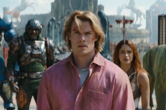 Young man in a pink shirt at center, with a woman behind him, amid armored soldiers and a large creature in a futuristic battlefield.