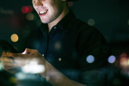 Happy young adult male using a smartphone in a night cityscape