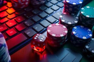 Stacks of colorful poker chips and a red dice sit on a backlit keyboard, suggesting online casino gambling.