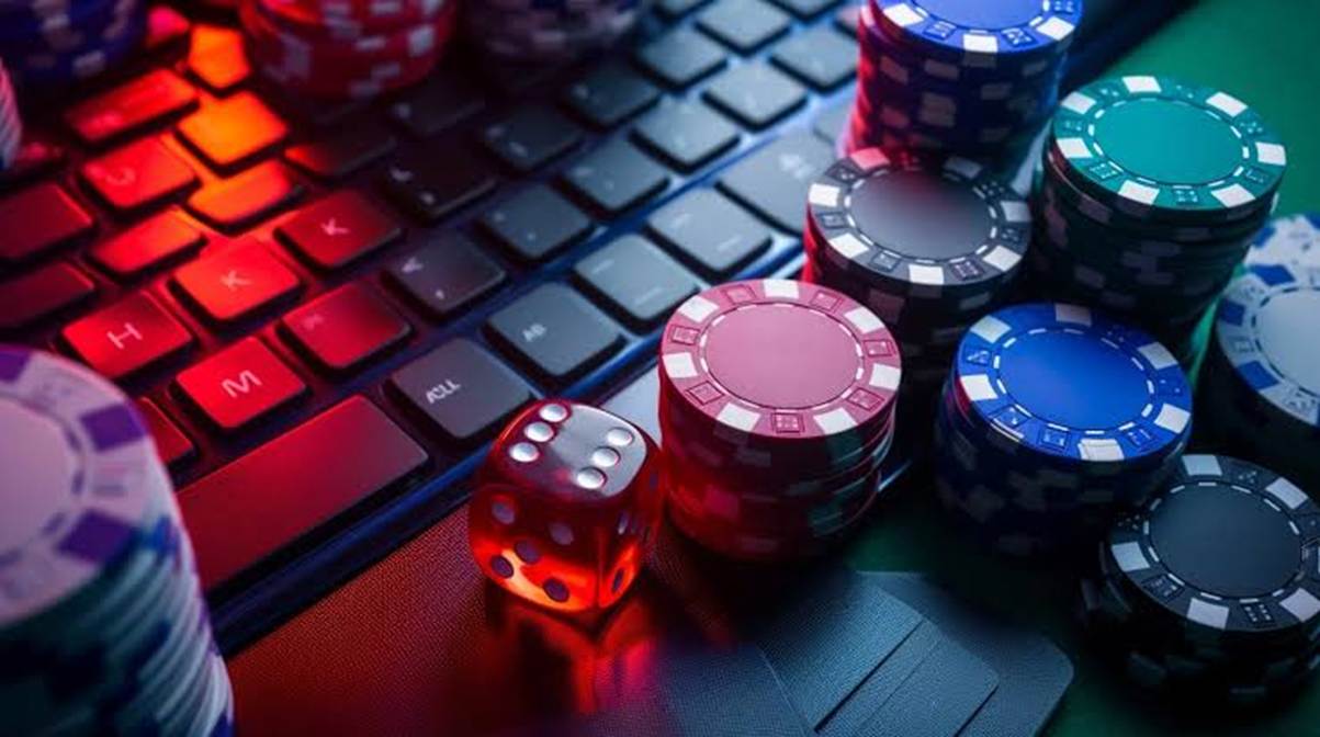 Stacks of colorful poker chips and a red dice sit on a backlit keyboard, suggesting online casino gambling.