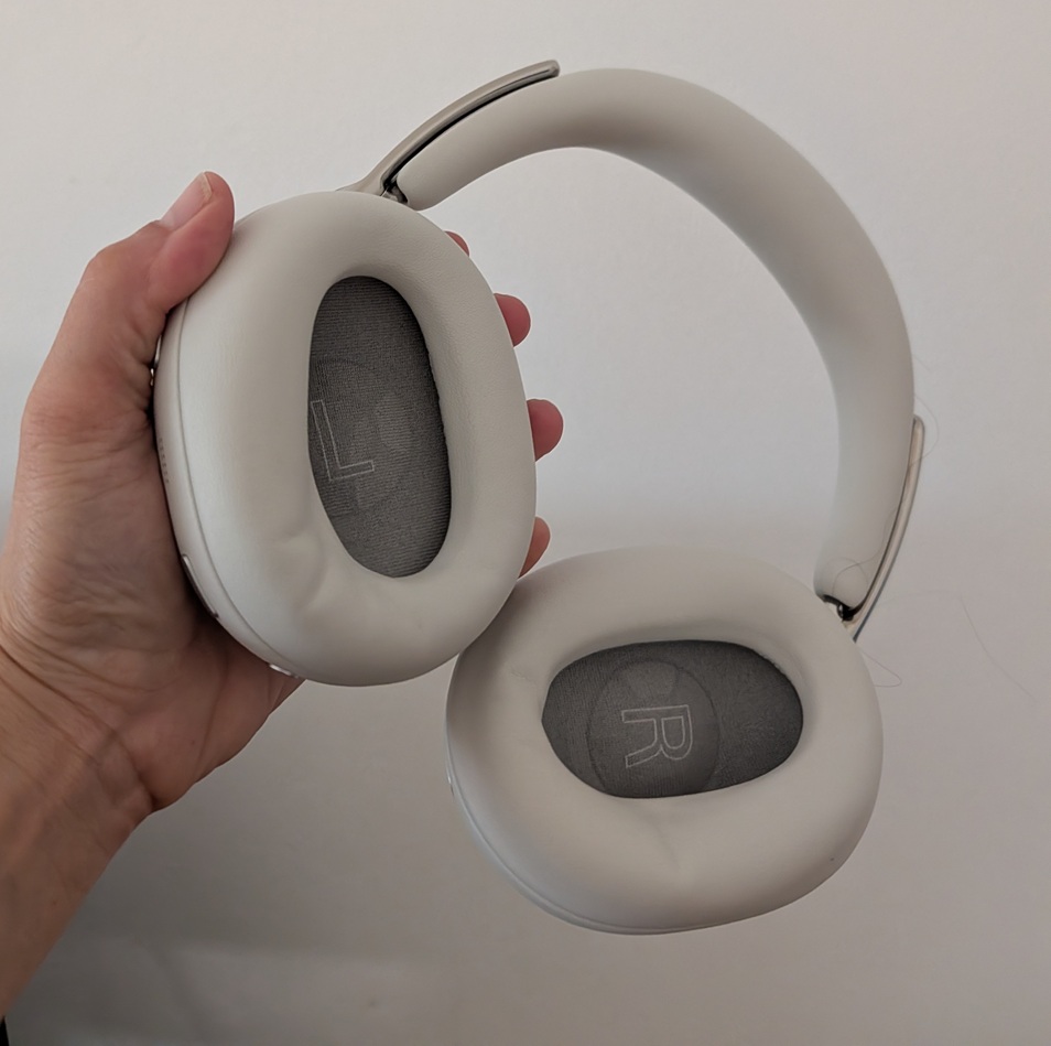 White over-ear headphones held in a hand, showing cushioned ear cups labeled L and R.