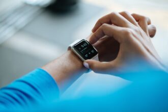 Person adjusts a white smartwatch on their left wrist over a blue sleeve.