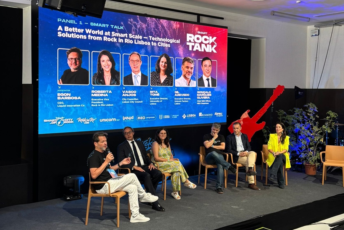 Panel discussion on a stage with six speakers seated; a large blue promotional screen behind them displays headshots and names for a 'Rock Tank' event.