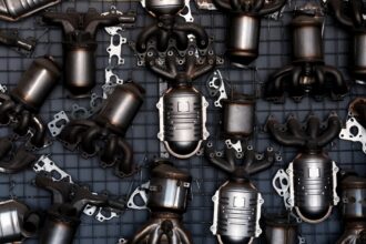 A dense arrangement of car exhaust parts, including catalytic converters and exhaust manifolds, laid out on a metal grid.