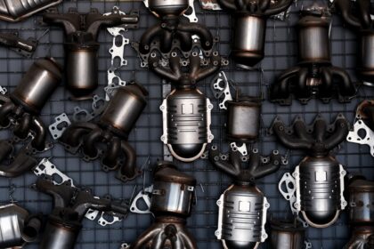 A dense arrangement of car exhaust parts, including catalytic converters and exhaust manifolds, laid out on a metal grid.