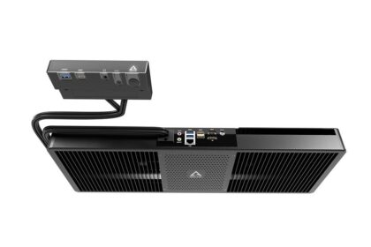 Black mini PC with a large ventilated front, connected to a small external I/O box via two cables.