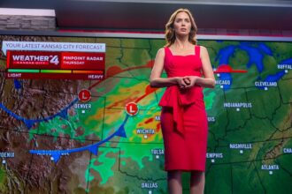 Female weather presenter in a red dress standing in front of a weather map with storm symbols and forecast graphics.