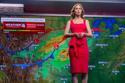 Female weather presenter in a red dress standing in front of a weather map with storm symbols and forecast graphics.