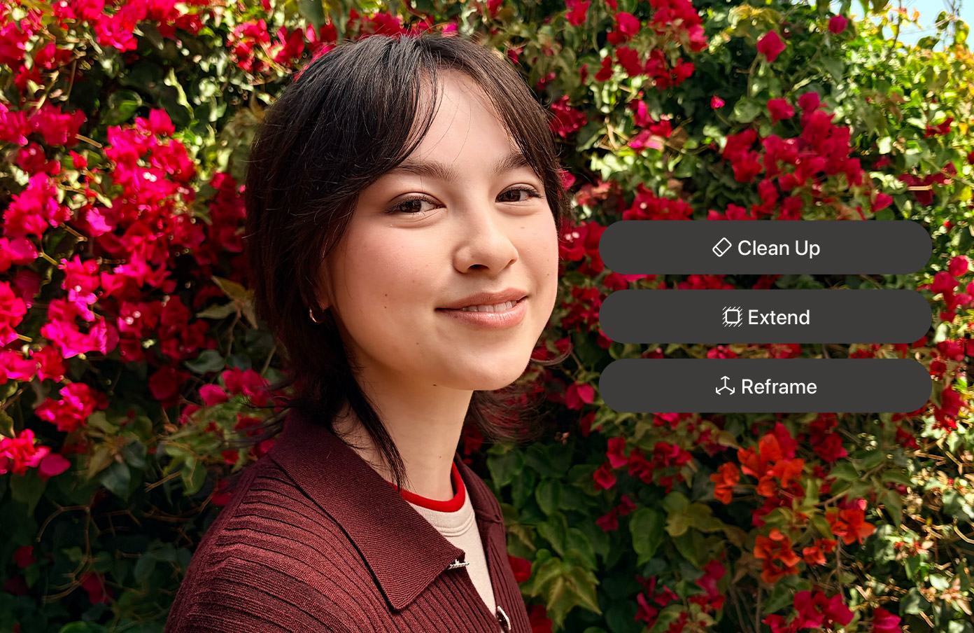 Portrait of a smiling woman with short dark hair, in a burgundy jacket, standing in front of bright pink bougainvillea with on-screen edit buttons (Clean Up, Extend, Reframe).
