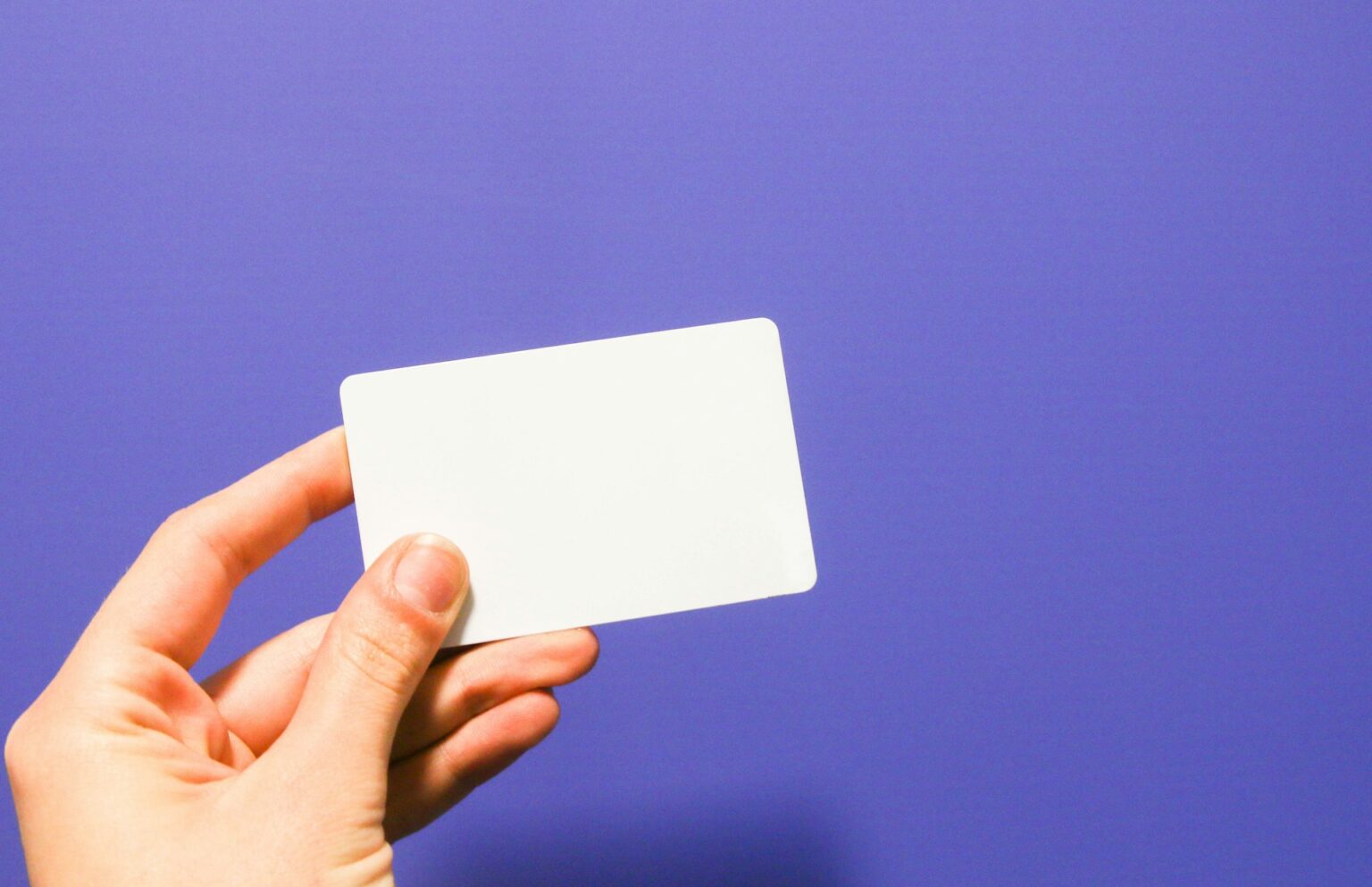 Close-up of a hand holding a blank white card against a solid purple background.