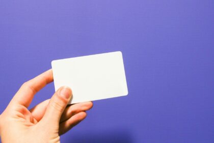 Close-up of a hand holding a blank white card against a solid purple background.
