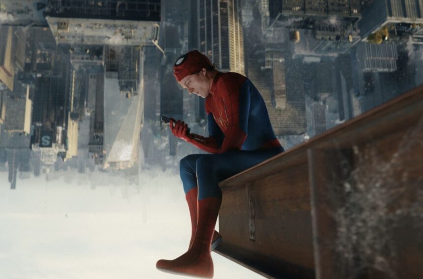 Spider-Man in red-blue suit sits on a rooftop ledge, looking at a smartphone above a vast cityscape below the skyline.