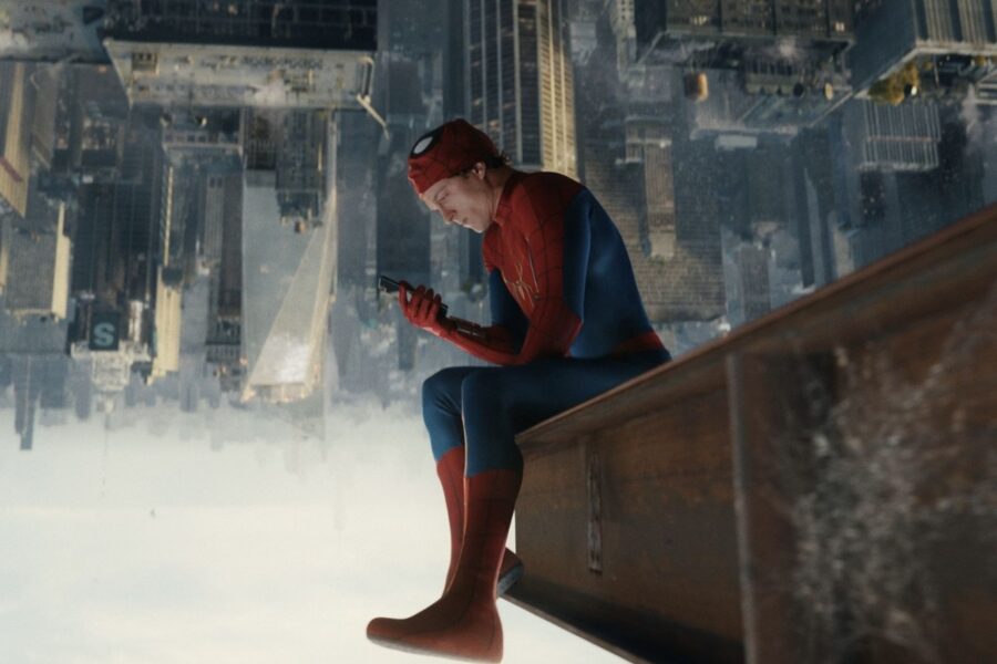 Spider-Man in red-blue suit sits on a rooftop ledge, looking at a smartphone above a vast cityscape below the skyline.