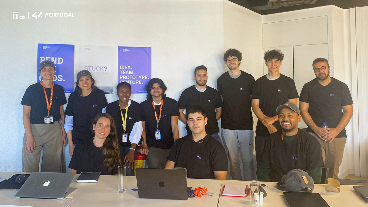 Group of staff in black t‑shirts posing for a team photo in a conference room with posters on the wall.