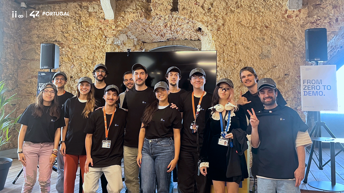 Group of people in black shirts posing for a group photo at a Portugal tech event, with a 'From Zero to Demo' sign in the background and a rustic wall behind them.