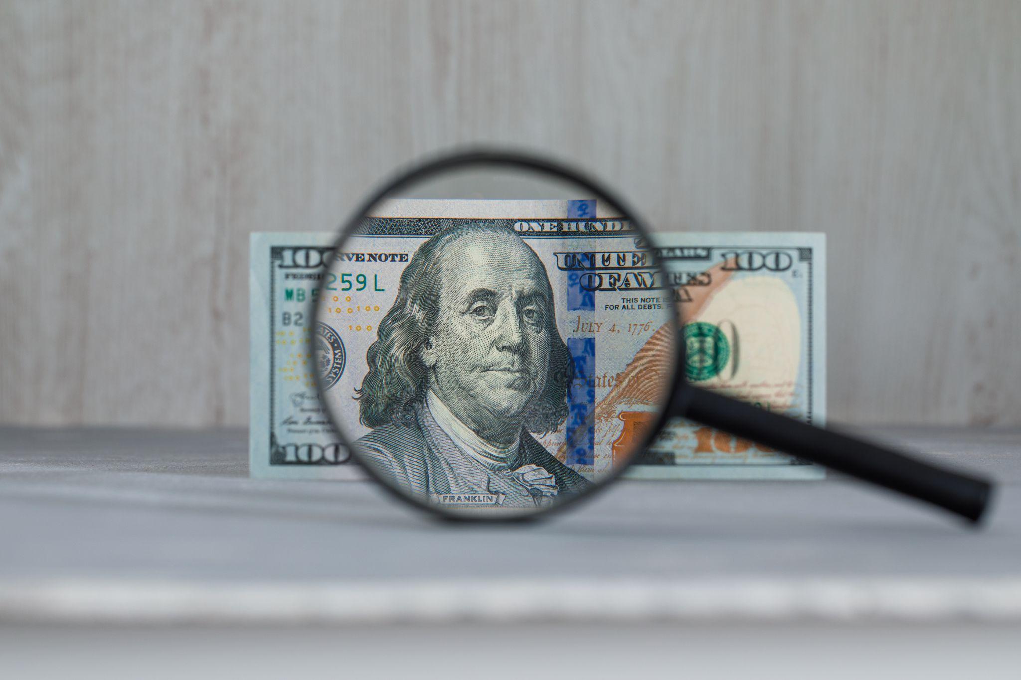 Magnifying glass over a US 0 bill, focusing on Benjamin Franklin's portrait.