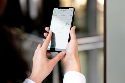 Person holding a smartphone displaying a stock chart with green candlesticks and a price, viewed up close