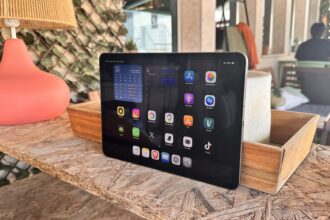 Tablet on a wooden table outdoors displaying app icons on the home screen (cafe-style setting).','Close-up of a tablet showing apps like App Store, Photos, Instagram on a patio table.','Tablet resting on a rustic wooden table with a pink lamp beside it, outdoor seating in the background.','Outdoorsy workspace: tablet with colorful app icons on a wood table and a woven lampshade nearby.','A tablet on a weathered wooden table beside a pink lamp, with blurred seating in the background.