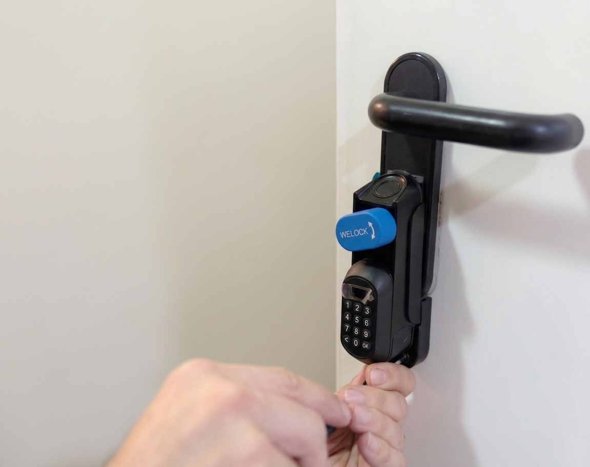 Person turning a door lock with a numeric keypad on a white door; blue WELOCK cover sits over the lock handle.