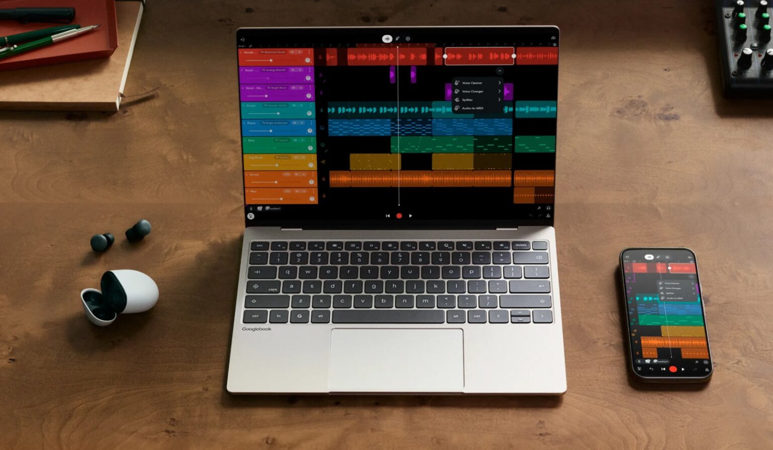 Laptop shows a colorful digital audio workstation with a track timeline on a wooden desk, with a smartphone displaying the same app nearby.