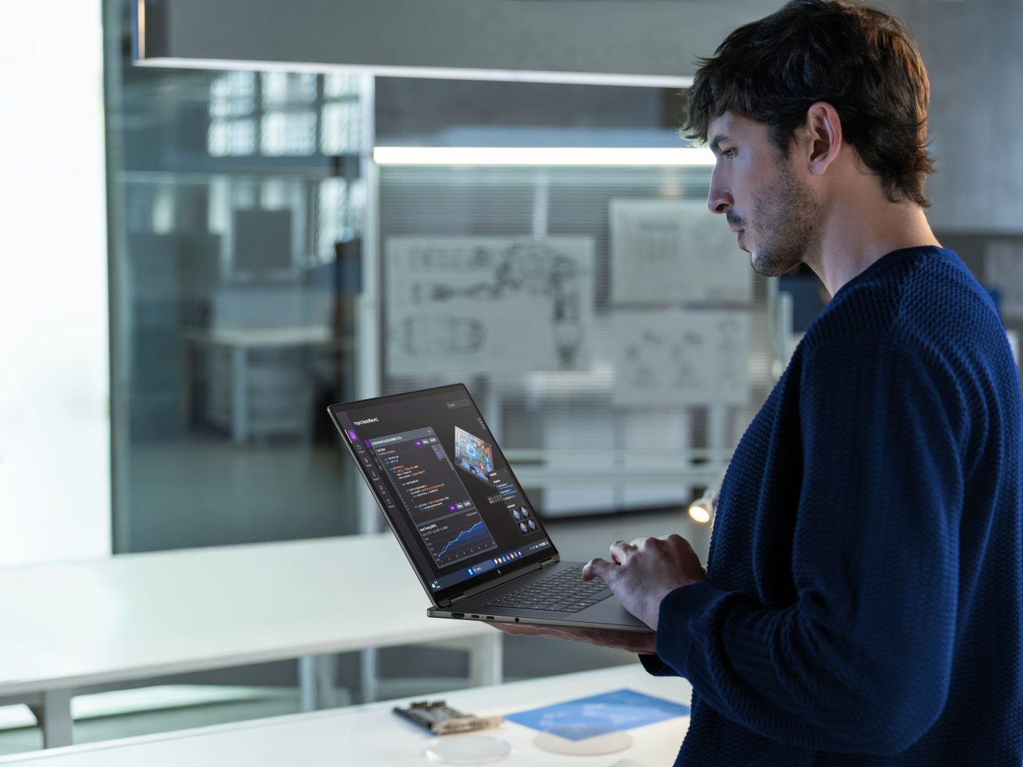 Engineer standing at a white desk, typing on a laptop displaying code in a modern office.