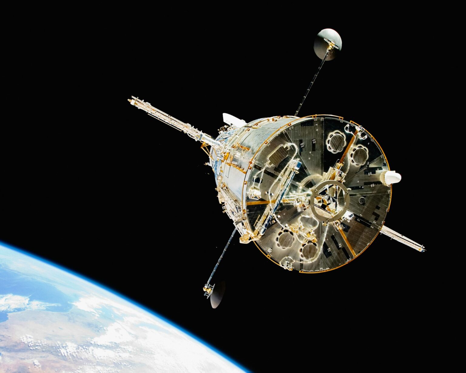 Spacecraft in orbit with a round hull and extended truss, set against the blackness of space and Earth's curved horizon below.