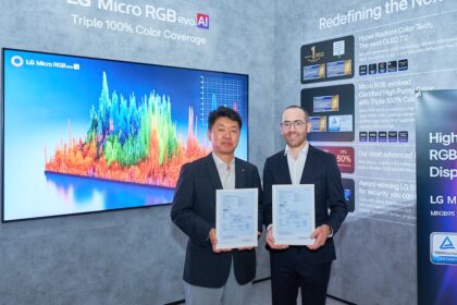 Two men in business suits hold framed certificates at an LG booth during a display launch event, with a large colorful screen behind them.