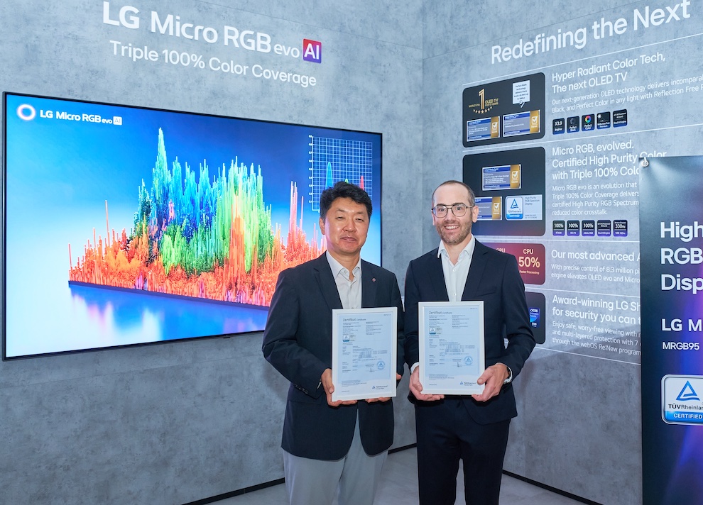 Two men in business suits hold framed certificates at an LG booth during a display launch event, with a large colorful screen behind them.