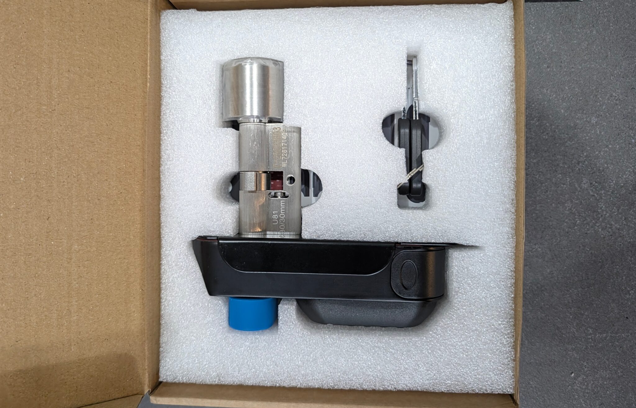 Industrial valve assembly with a cylindrical metal body and a blue knob, secured in foam padding inside a cardboard box.