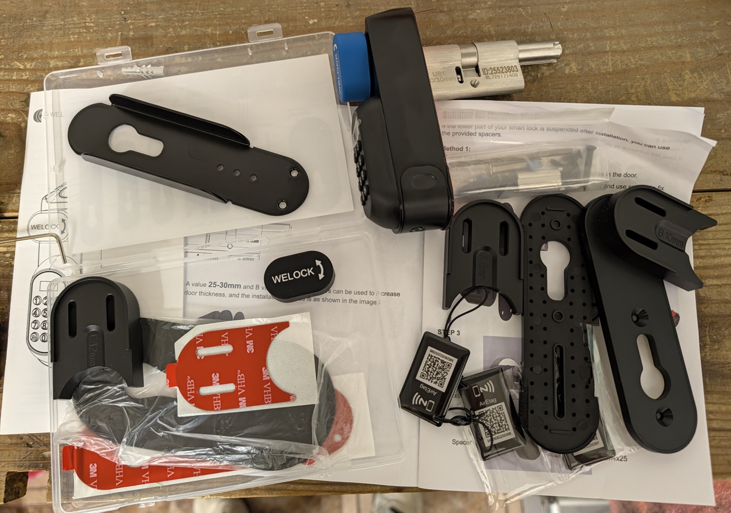 Disassembled smart door lock kit parts including mounting brackets, screws, and instruction sheets on a wooden table.