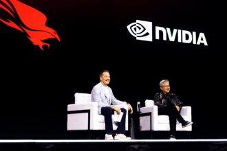 Panel discussion on a dark stage with two men seated in white chairs; a large NVIDIA logo and red dragon graphic loom in the background, suggesting a tech event.