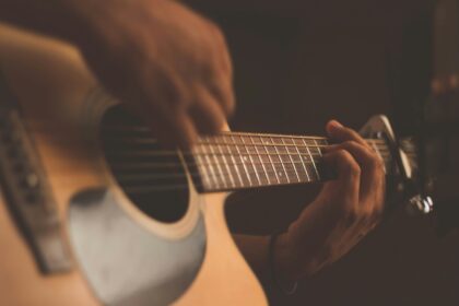 Close-up of hands on the fretboard of an acoustic guitar in warm lighting.