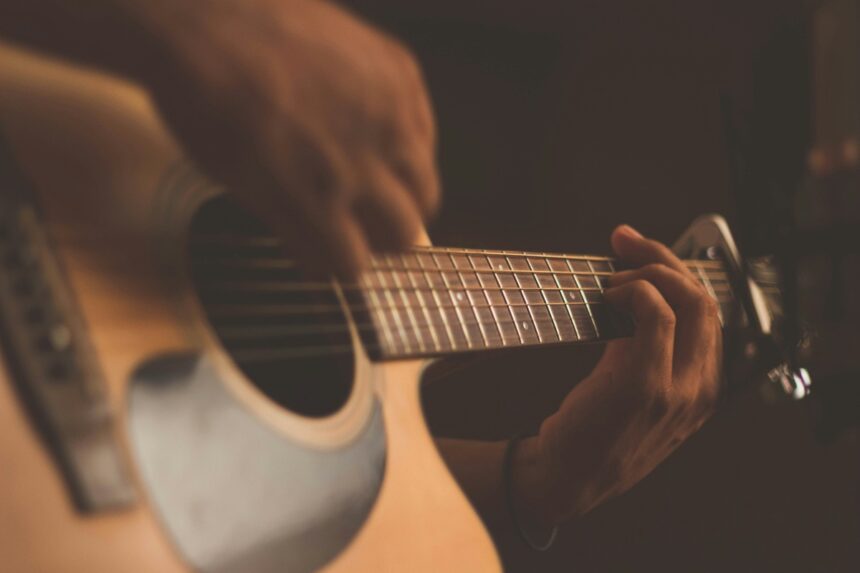 Close-up of hands on the fretboard of an acoustic guitar in warm lighting.