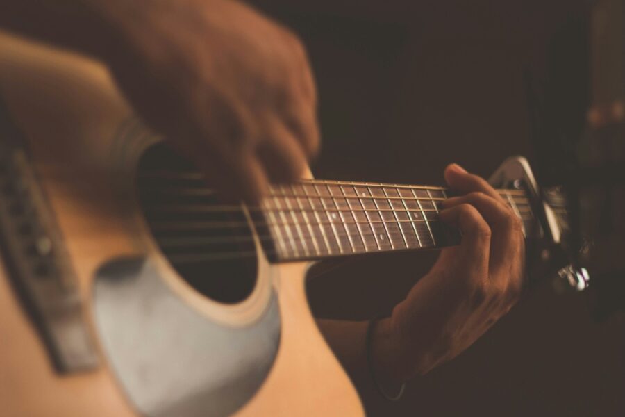 Close-up of hands on the fretboard of an acoustic guitar in warm lighting.