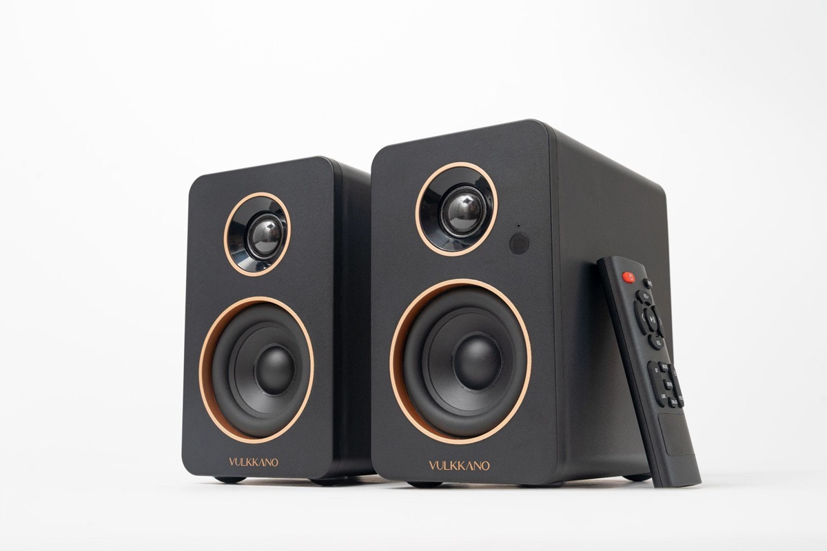 Pair of black bookshelf speakers with copper rings around the drivers and the VULKKANO logo, plus a remote on the right.