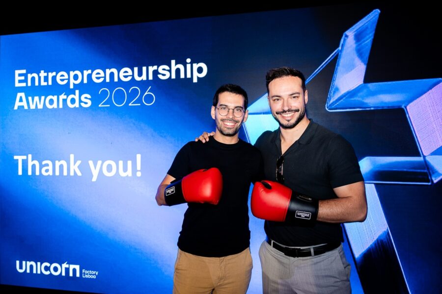 Two men in black shirts wearing red boxing gloves pose together in front of a blue Entrepreneurship Awards 2026 backdrop.