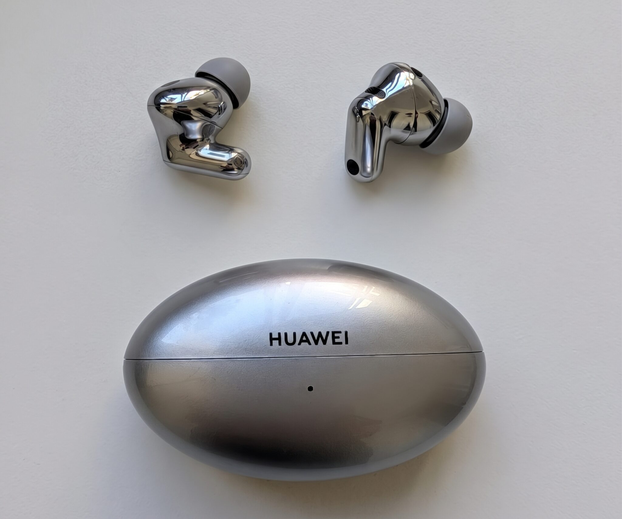 Pair of metallic Huawei wireless earbuds with gray silicone tips, mounted above a round Huawei charging base/ears display.