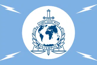 Interpol emblem featuring globe, sword, and scales on a white circle against a blue background.