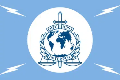 Interpol emblem featuring globe, sword, and scales on a white circle against a blue background.