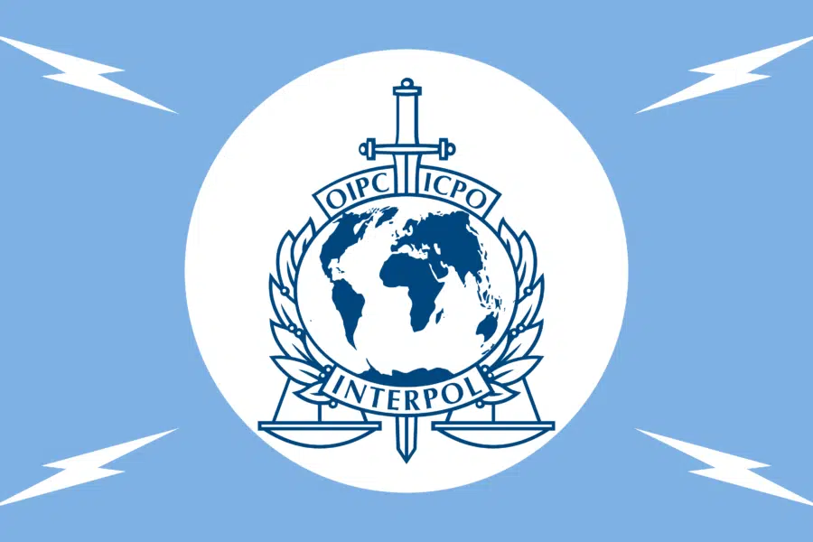 Interpol emblem featuring globe, sword, and scales on a white circle against a blue background.