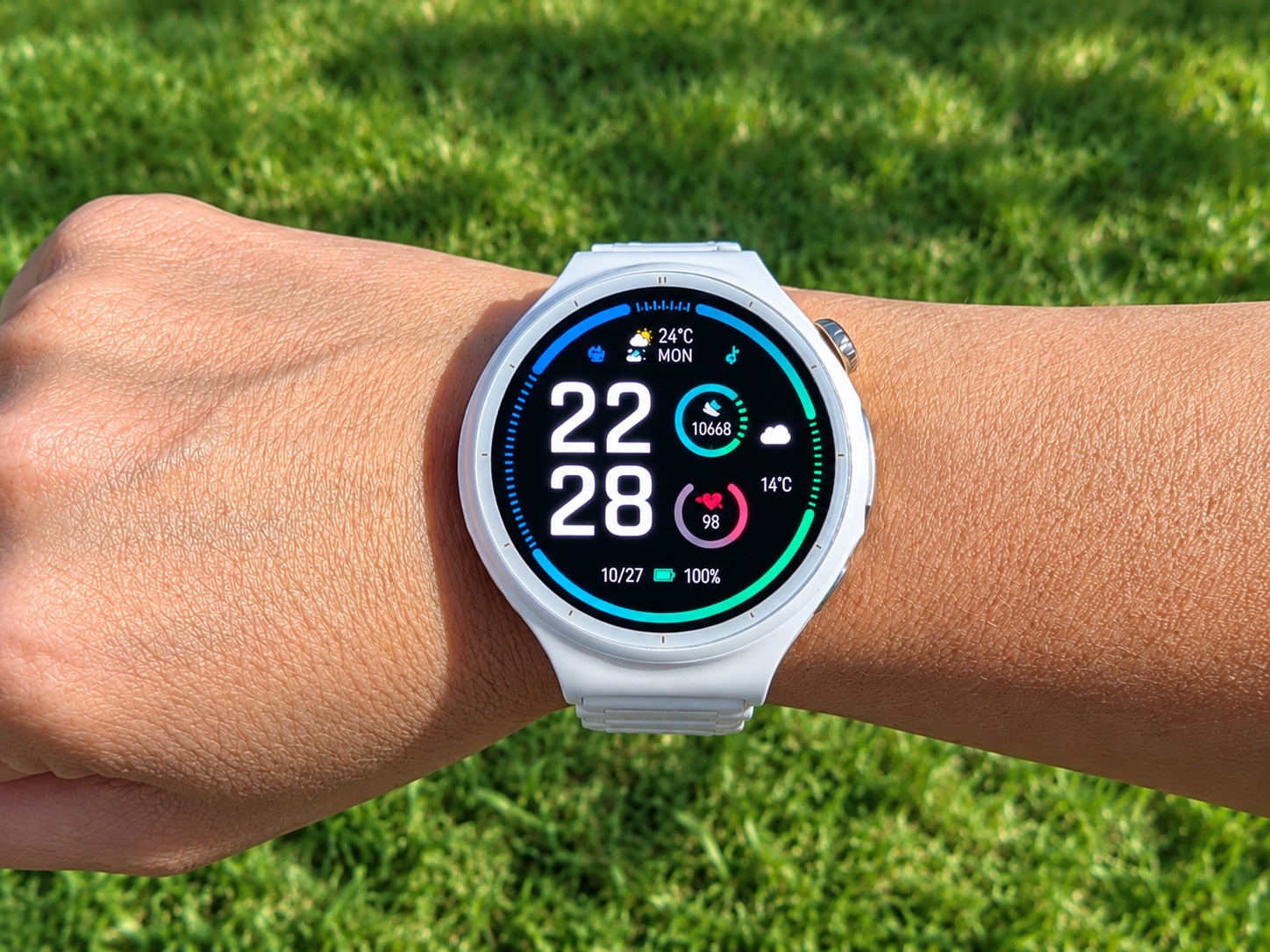 Smartwatch on a wrist displaying time 22:28 and fitness metrics against a grassy background